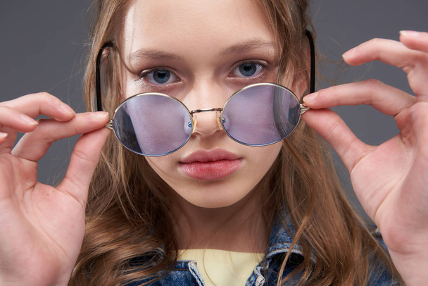 Beautiful teenage girl taking off blue round glasses - Photo, Image