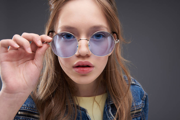 Beautiful teenage girl touching frame of blue round glasses - Photo, Image
