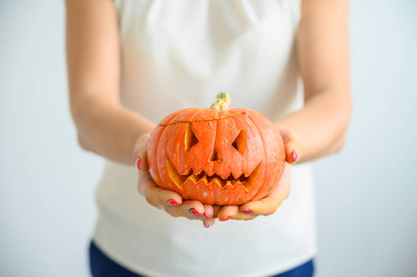 A woman in a white blouse holds a pumpkin for Halloween. Close-up of female hands with a lantern jack on a white background on the eve of All Saints. foreground. Trick or treat. Scary grimace. - Foto, Imagem