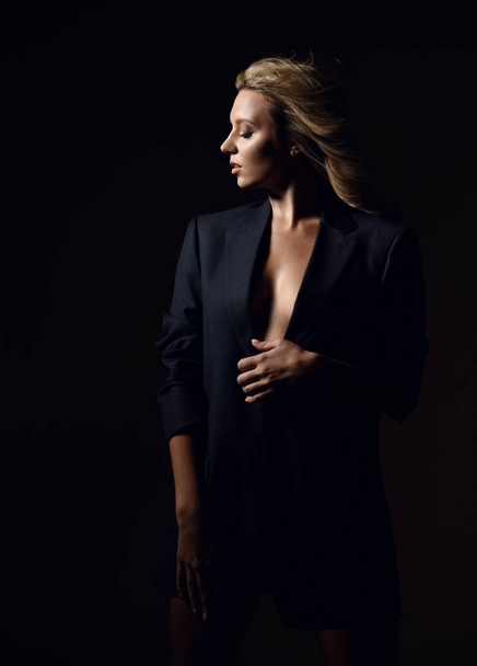 Young sensual blonde woman in mens suit jacket over her naked body is standing in the wind holding jacket - Fotoğraf, Görsel