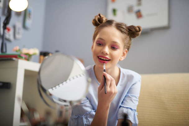 Charming teen girl applying red lipstick with brush - Foto, afbeelding