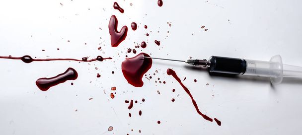 Seringue et éclaboussures de sang sur fond blanc. Beaucoup de sang et une seringue
. - Photo, image