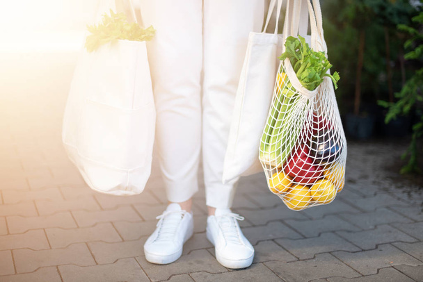 Zero waste concept with copy space. Woman holding cotton shopper and reusable mesh shopping bags with vegetables, products. Eco friendly mesh shopper. Zero waste, plastic free concept. - Foto, imagen