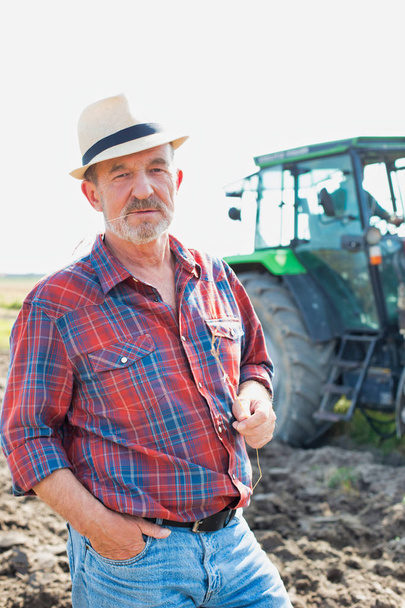 Portrait of confident senior farmer standing against tractor at farm - 写真・画像