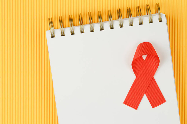 red aids ribbon on open notebook isolated on yellow background - Photo, Image