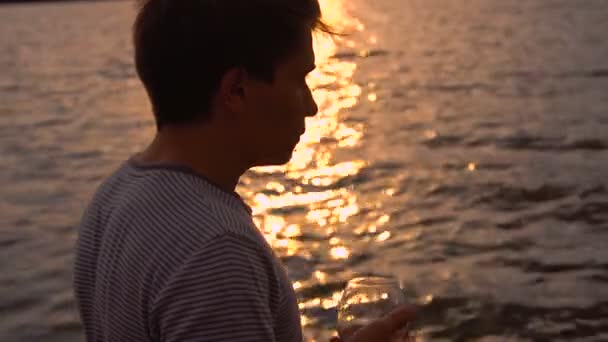 Człowiek picia butelkę wina podczas zachodu słońca w pobliżu morza, w zwolnionym tempie - Materiał filmowy, wideo