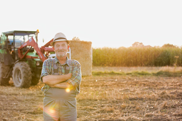Portrait of confident senior farmer standing against tractor at farm - Foto, imagen