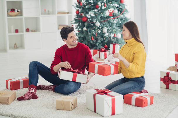 Full size profile side photo of two romantic people hold gift box get presents from santa claus sit on floor in house with evergreen tree x-mas noel decoration - Foto, immagini