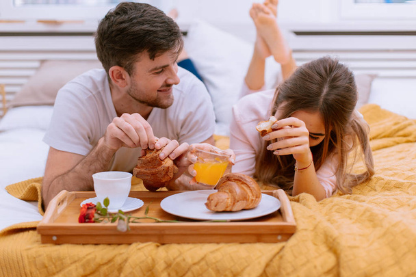 Un couple s'assoit sur le lit et sert le petit déjeuner ensemble
 - Photo, image