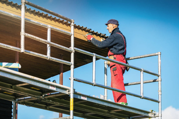человек на строительных лесах устанавливает новые деревянные доски на крыше дома ea
 - Фото, изображение