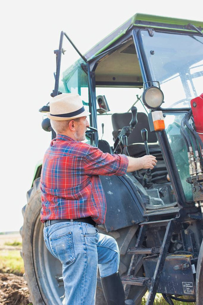 Portrait of confident senior farmer opening tractor at farm - Фото, изображение