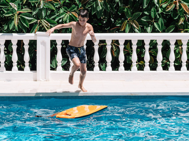 Pre-teens dengelerini korumak için küçük bir sörf tahtası üzerinde atlayarak havuzda oynamak. - Fotoğraf, Görsel