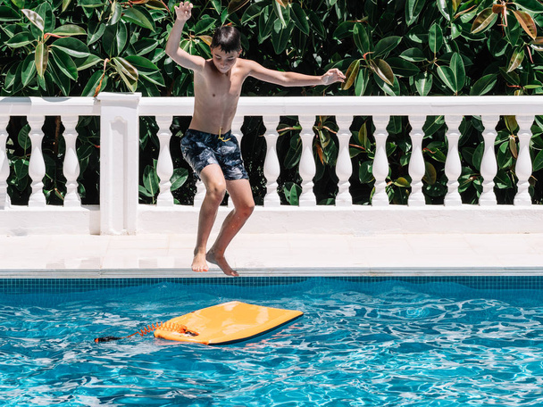 Pre-teens play in the pool by jumping on a small surfboard to keep their balance. - Foto, afbeelding