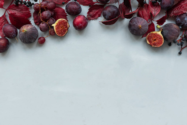 Border of purple girlish (wild) grape leaves, grapes, plums and figs on gray wooden background. Top view. Flat lay. Autumn harvesting or Thanksgiving celebration concept. - Photo, image