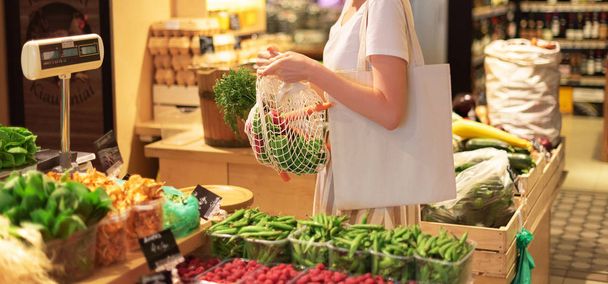 Woman chooses fruits and vegetables at farmers market. Zero waste, plastic free concept. Sustainable lifestyle. Reusable cotton and mesh eco bags for shopping. - Photo, image