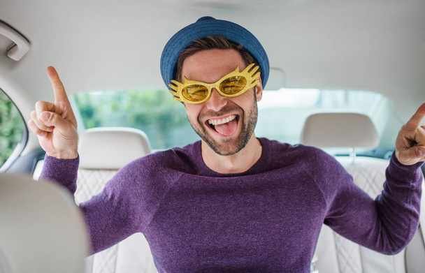 Cheerful man with party accessories sitting in car, having fun. - Foto, imagen