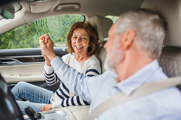 Feliz pareja de ancianos con teléfono inteligente sentado en el coche, hablando
. - Foto, Imagen