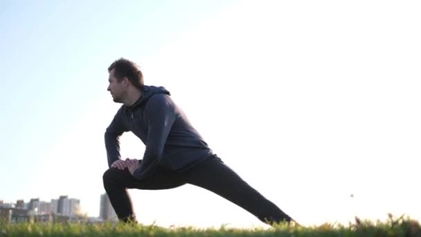 Fiatal kaukázusi Férfi sportoló stretching lábak parkban - Felvétel, videó