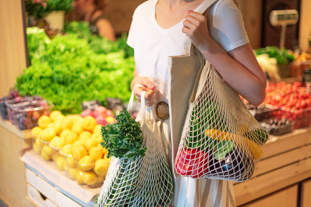 Girl holding mesh shopping bag and cotton shopper with vegetables without plastic bags, wooden background. Zero waste, plastic free concept. Sustainable lifestyle. Banner. - Фото, зображення