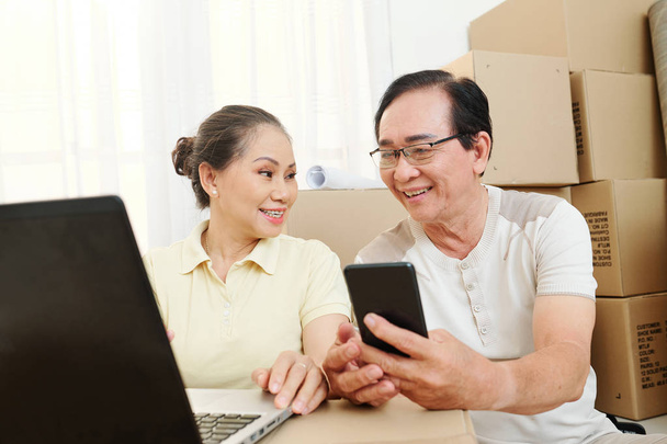 Heureux couple vietnamien senior travaillant sur ordinateur portable et discuter des détails du déménagement
 - Photo, image