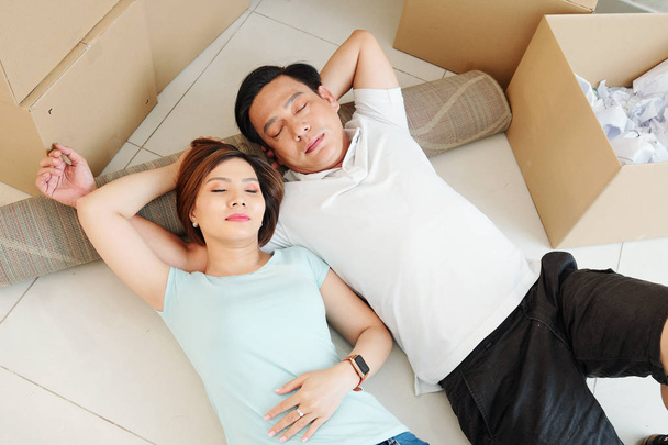 Asian couple tired of packing sleeping on the floor in living room with boxes  - Photo, Image