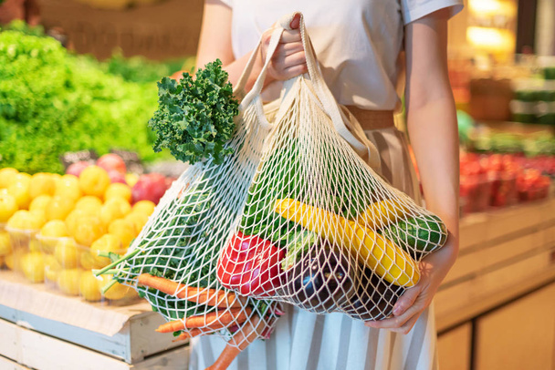 Zero waste concept with copy space. Woman holding cotton shopper and reusable mesh shopping bags with vegetables, products. Eco friendly mesh shopper. Zero waste, plastic free concept. - 写真・画像
