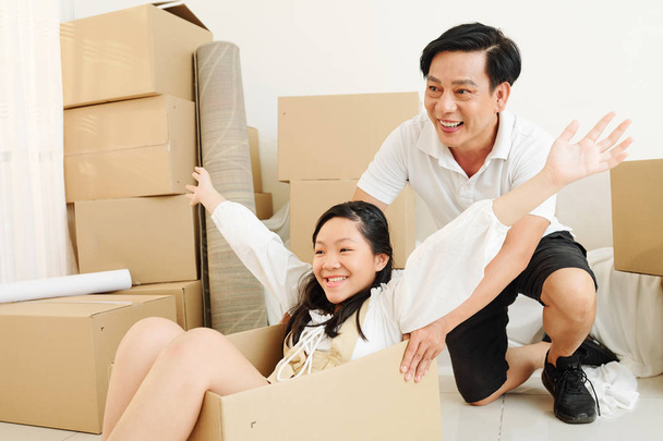 maduro asiático hombre empujando caja con su bastante preadolescente hija sentado dentro después de que se mudaron en nueva casa
 - Foto, imagen