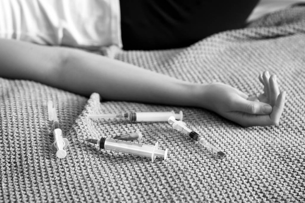 Zwart-wit foto van jonge bewusteloze vrouw met spuiten liggend op bed. Suicide concept - Foto, afbeelding