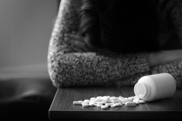Черно-белое фото депрессивной женщины возле кучи таблеток на столе дома
 - Фото, изображение