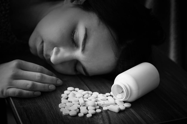 Musta ja valkoinen kuva nuoresta tajuttomasta naisesta, jolla on pillereitä pöydällä. Itsemurhan käsite
 - Valokuva, kuva