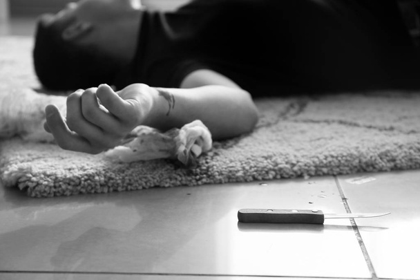 Μαύρη και λευκή φωτογραφία νεκρού άντρα με κομμένες φλέβες στο πάτωμα. Έννοια της αυτοκτονίας - Φωτογραφία, εικόνα