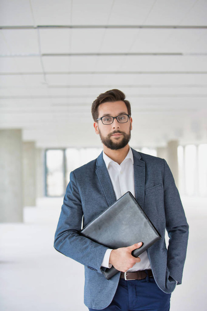 Portrait of attractive beaded businessman wearing glasses and holding folder - Foto, Imagem