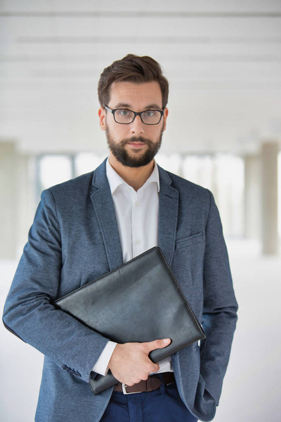 Portrait of attractive beaded businessman wearing glasses and holding folder - 写真・画像