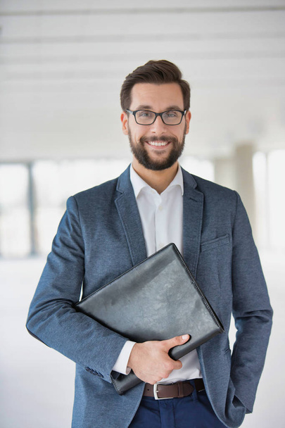 Portrait of attractive beaded businessman wearing glasses and holding folder - Fotó, kép