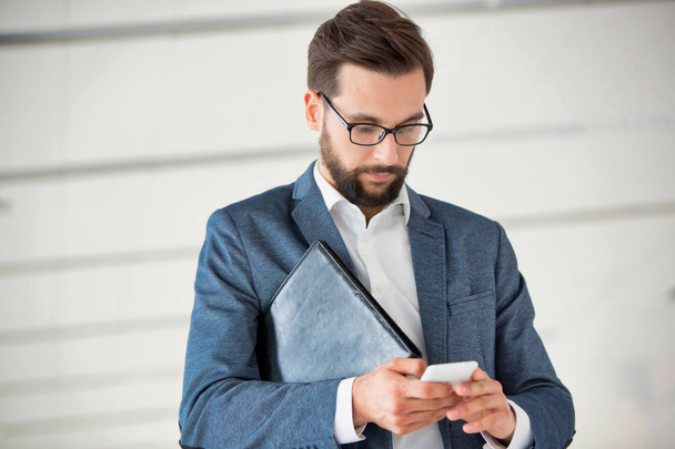Attractive bearded businessman using smart phone in office - Foto, Imagen