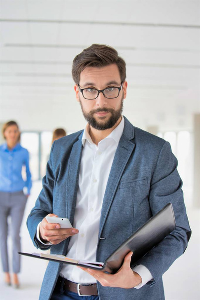 Attractive bearded businessman using smart phone in office - Foto, afbeelding