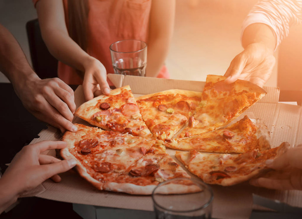 Jongeren plakjes warme smakelijke pizza uit kartonnen doos - Foto, afbeelding