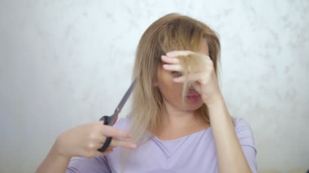 concept of damaged long hair. blond woman cuts hair ends with scissors. - Imágenes, Vídeo