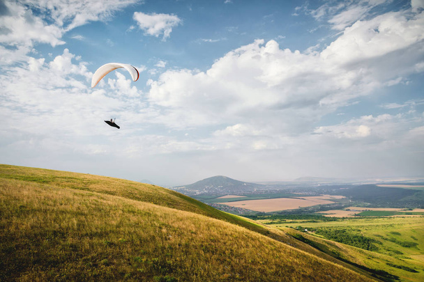 A white-orange paraglider flies over the mountainous terrain - Foto, Bild