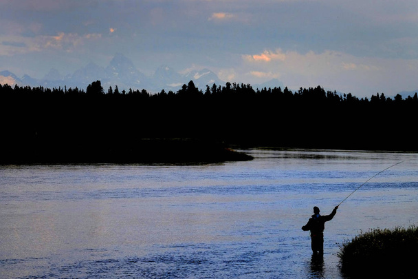Pêcheur volant sur la rivière avec des tonnes en arrière-plan
 - Photo, image