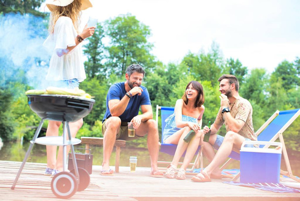 Woman preparing food in barbecue grill with friends on pier - Foto, Imagem