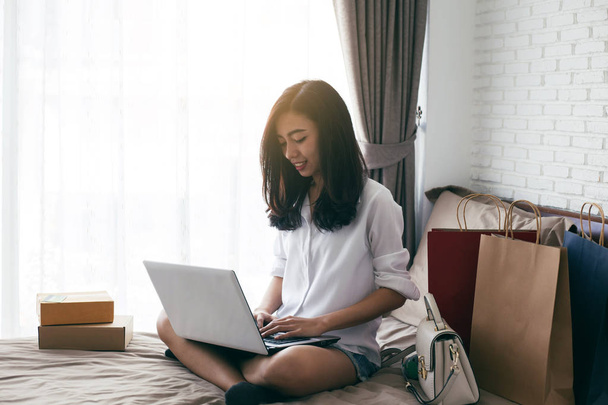 Woman using laptop computer on her bed, In the white bedroom by the window, shopping online concep - Photo, image