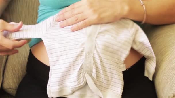 Zwanger meisje kijkt naar een baby jurk voor een pasgeboren baby. - Video