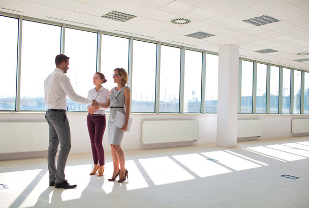 Young businessman greeting businesswoman with handshake standing by colleague in new office - Photo, image