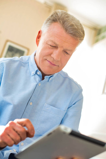 Mature man using digital tablet at home - Fotoğraf, Görsel
