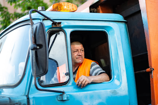 Водитель мусоровоза курит в кабине грузовика
 - Фото, изображение