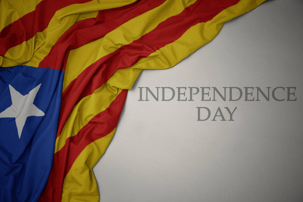 machając kolorowe flagi narodowej Katalonii na szarym tle z dniem niepodległości tekstu. - Zdjęcie, obraz