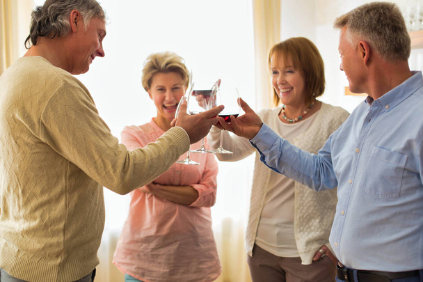 Smiling mature friends standing with drinks at home - Фото, изображение