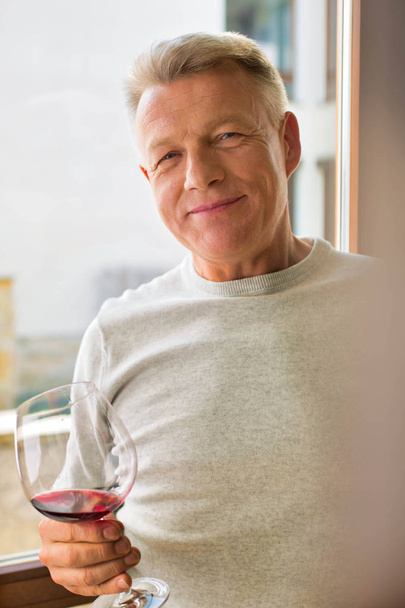 Portrait of mature man holding wineglass standing at home - Foto, Bild