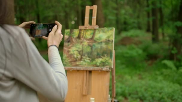 ブルネットの女性のバックビューは、森の中のオープンエアで風景をペイントし、写真を撮ります - 映像、動画